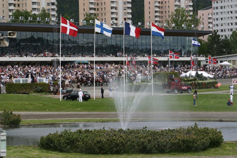 Travbane med noen flagg og mennesker. Sprinkler som vanner en busk.