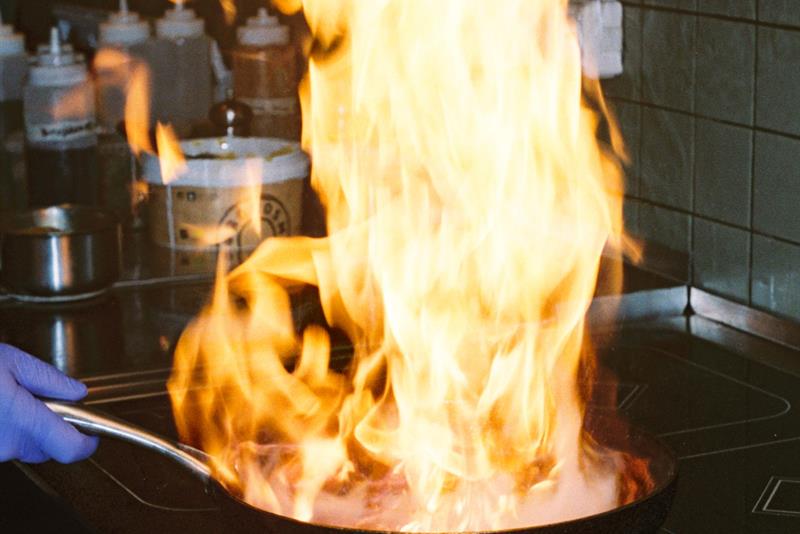 Flammene står opp fra en panne på koketoppen under matlaging i et profesjonelt restaurantkjøkken.
