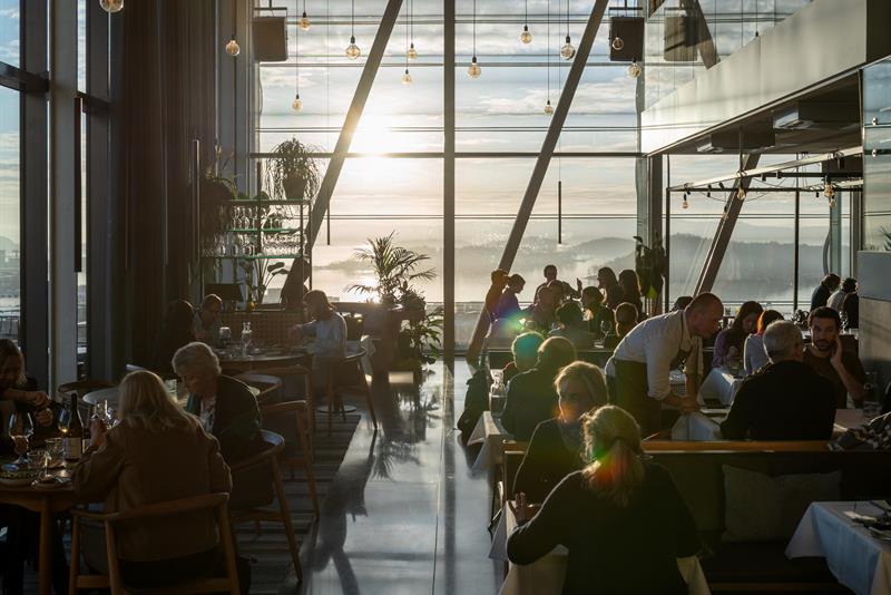 Folk spiser i en moderne restaurant med store panoramavinduer og utsikt over solnedgangen over Oslofjorden