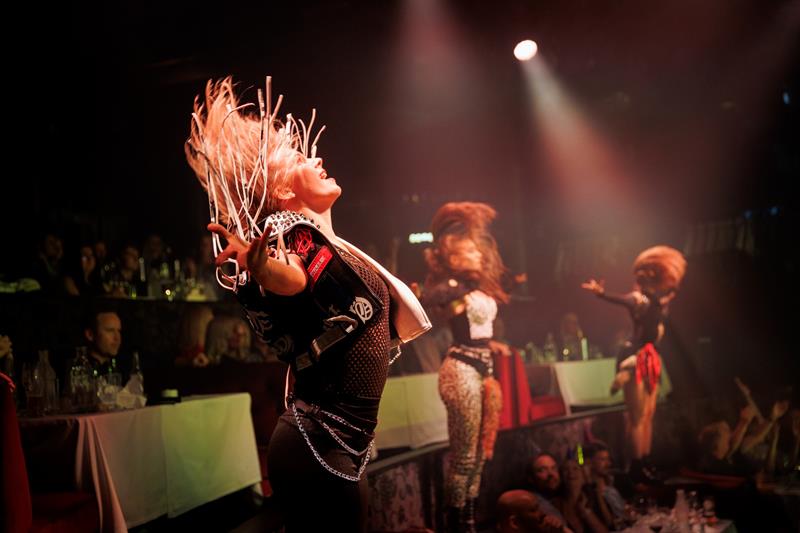 En dynamisk danser pisker håret i takt med rytmen under en intens sceneopptreden med publikum tett på. Scenen er full av energi og bevegelse.