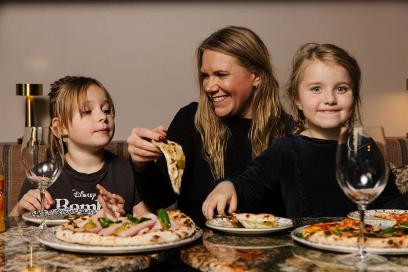 En kvinne og to unge jenter spiser pizza sammen