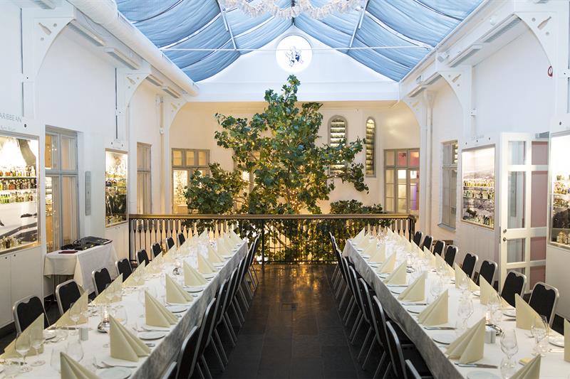 Festsalen med to langbord med hvite duker og et stort tre i bakgrunnen