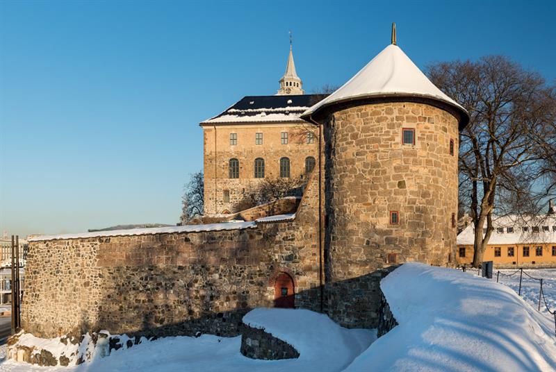 Vinterbilde av Munketårnet med slottet i bakgrunnen. Bakken er dekket av snø.