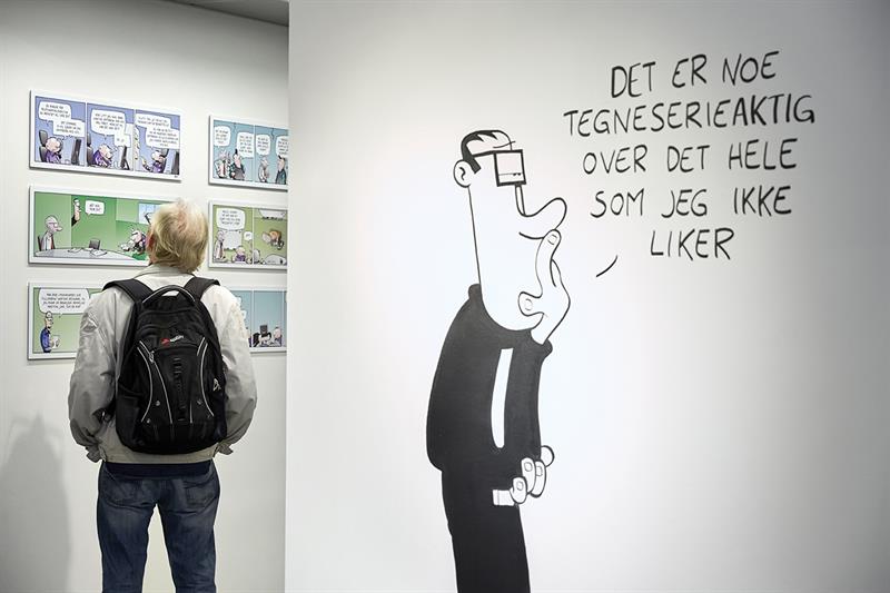 En mann ser på en tegneserieutstilling, og en tegneseriefigur er malt på veggen.