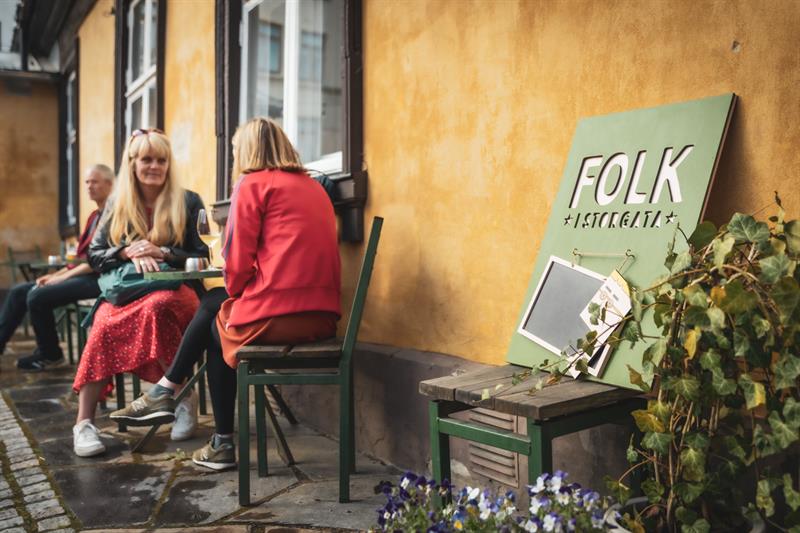 Velkomstskilt og folk som sitter på uteområdet med drinker