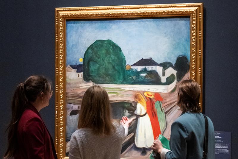 Tre jenter ser på maleriet "Jenter på en bro" av Edvard Munch.