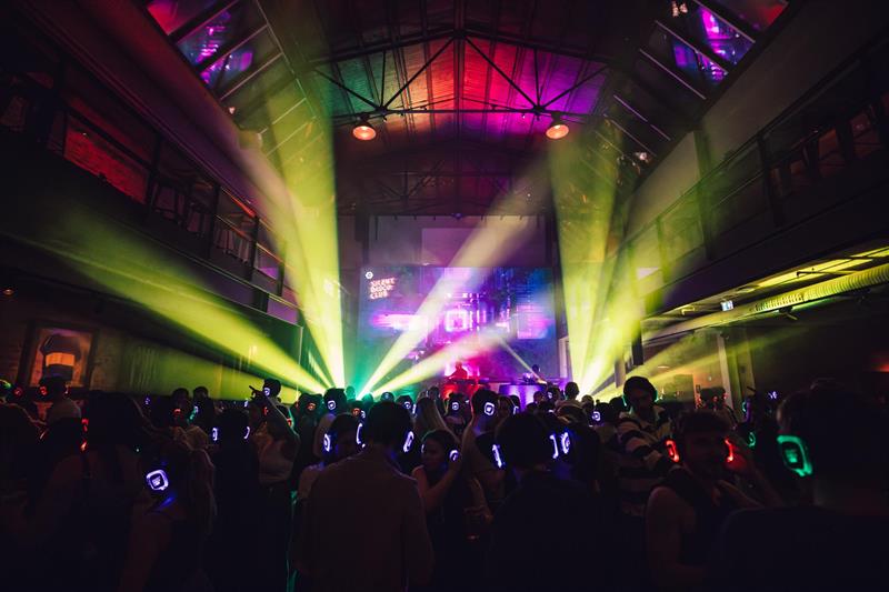 Silent disco-arrangement: Dansegulv fylt av folk med hodetelefoner og neonlys