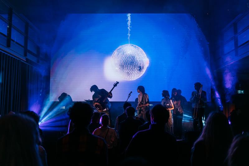 Band som spiller konsert foran publikum, under en stor discobolle