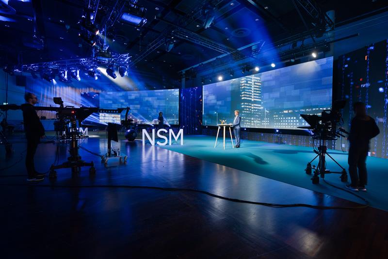 Programleder på en stor scene med kamerateam rundt seg