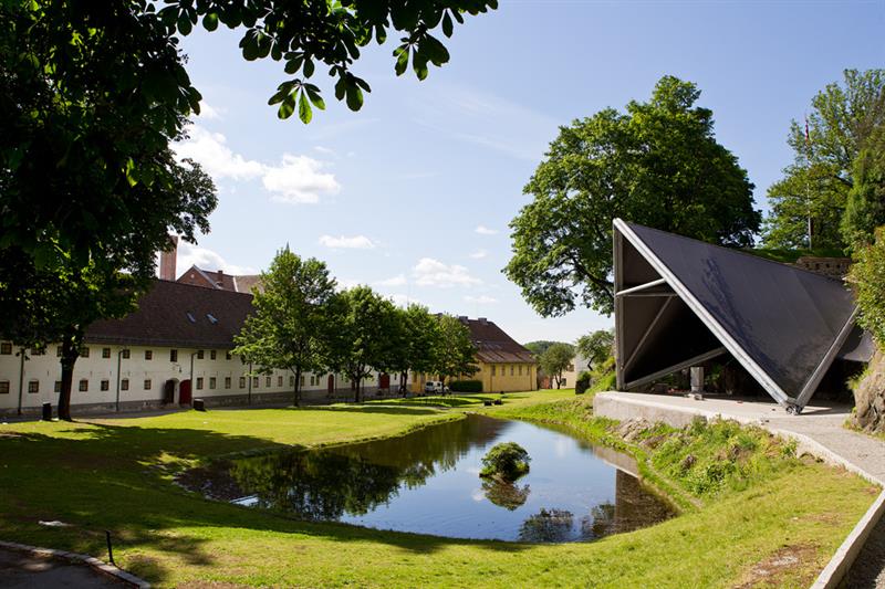 Dammen, plenen, scenen, trærne og den hvite bygningen bak festningen.