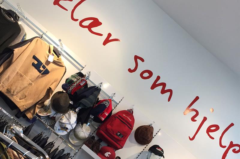 Ulike klær og vesker henger på veggen, teksten "Clothes that help" er malt på veggen.