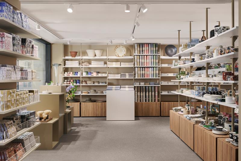Interiørfoto. Hyller med utstilling av designprodukter. Beige vegger, hvitt tak, grått gulv.