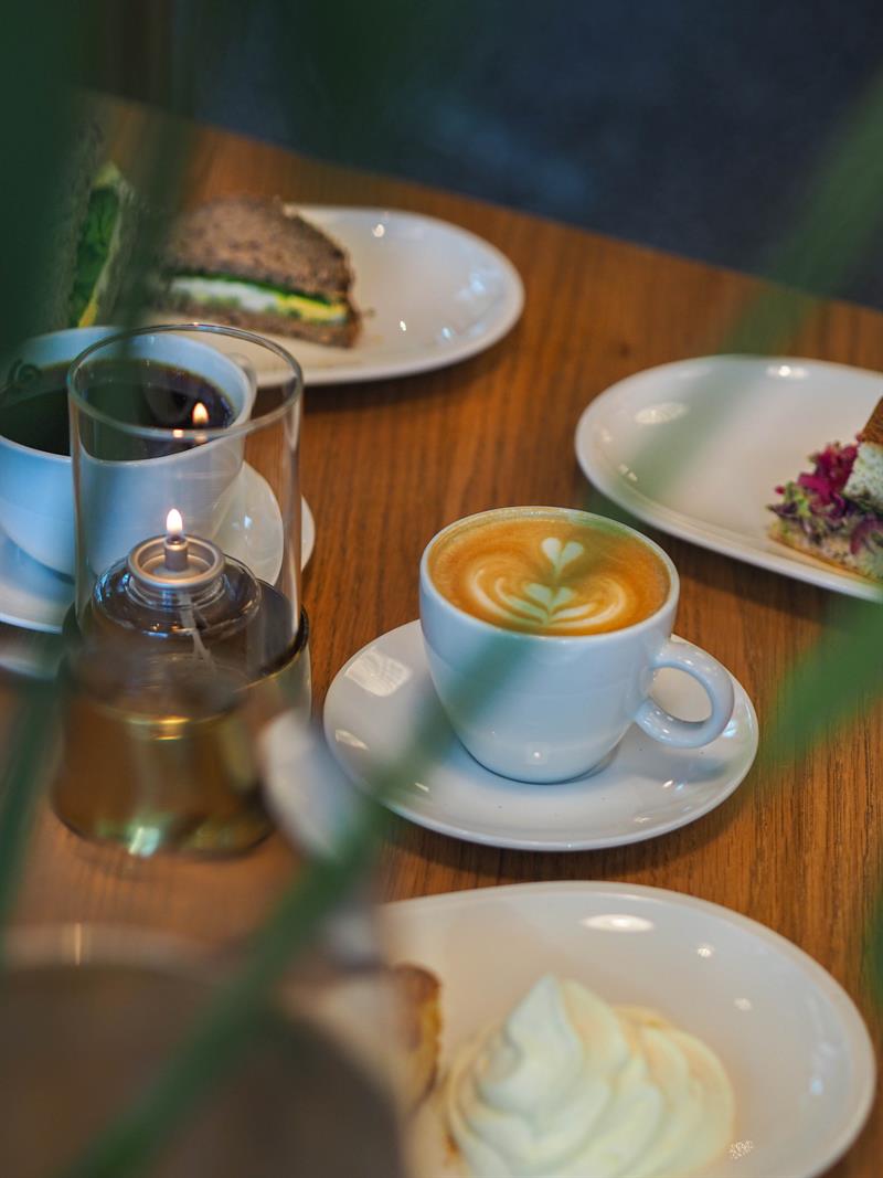 Tallerkener med brød og bakverk, kopp med cappuccino og kopp med svart kaffe