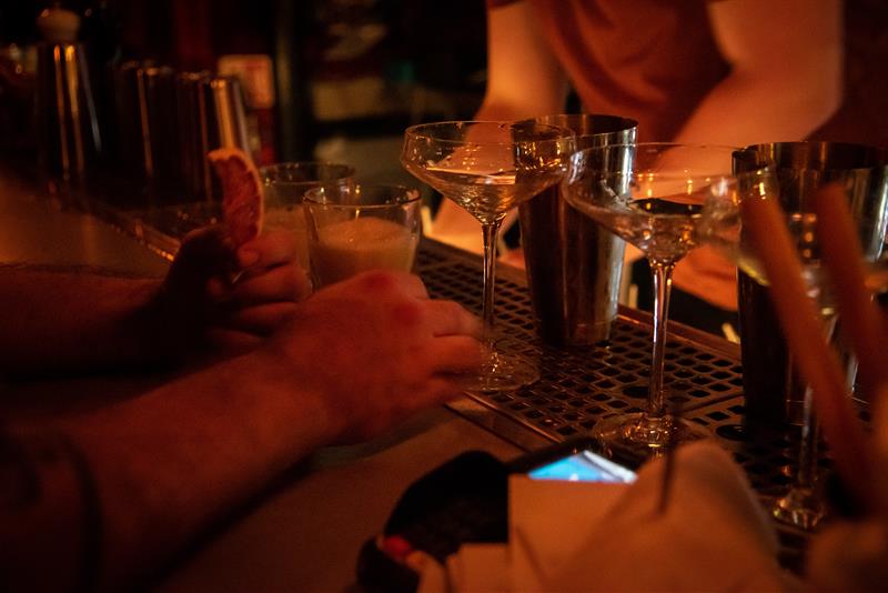 Nærbilde av ulike hender og drinker på en bardisk.