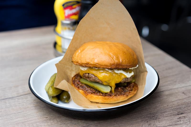 Detaljbilde av en cheeseburger med sylteagurk på en hvit tallerken.