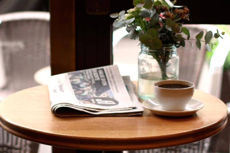 Detaljbilde av en avis, en potteplante og en kaffekopp.