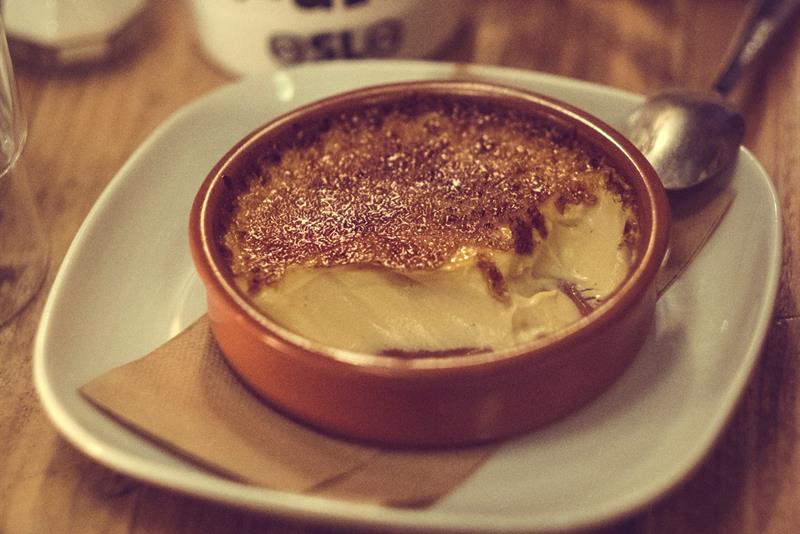 En kremet dessert som serveres i et lite fat med kaffe ved siden av på et trebord.