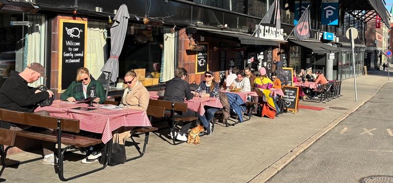 Gjestene sitter ute i solen på en livlig fortausplass foran Den Glade Gris i Oslo.