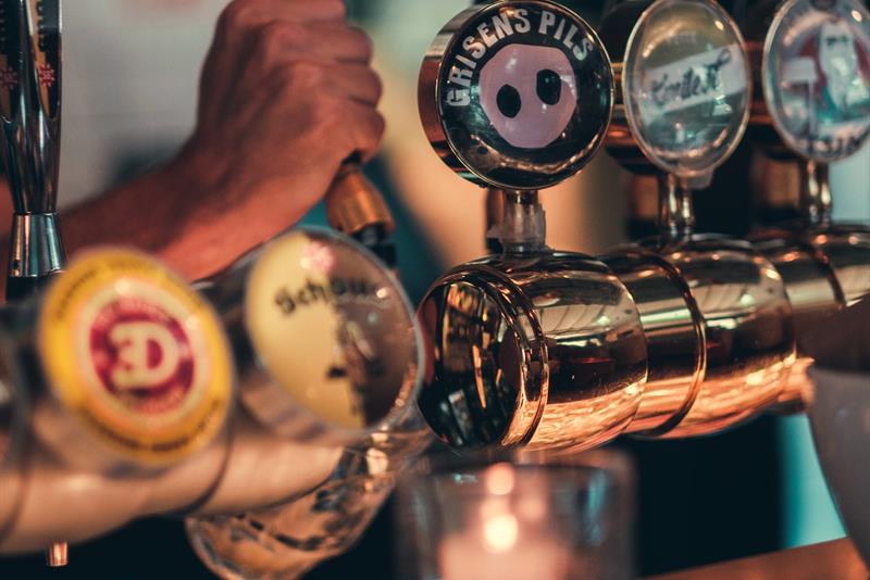 En bartender skjenker øl fra polerte kraner i en koselig og stemningsfull bar.