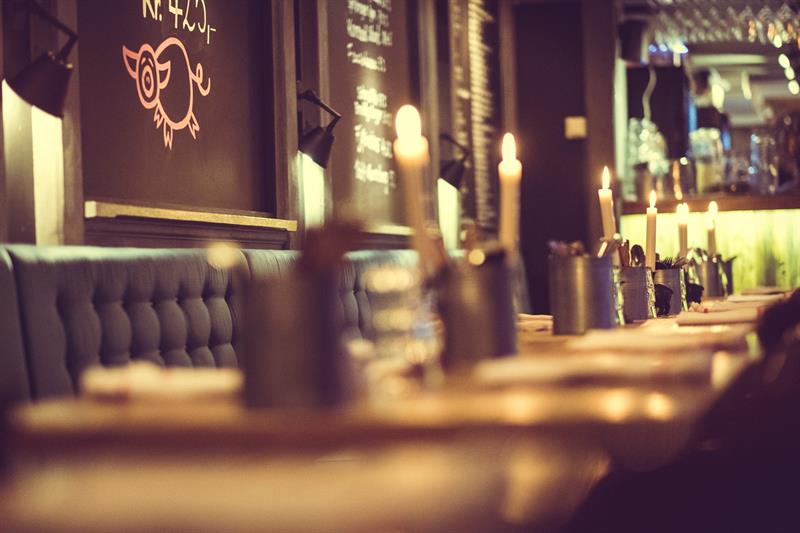 Et koselig restaurantinteriør med tente stearinlys og et langbord som er dekket.
