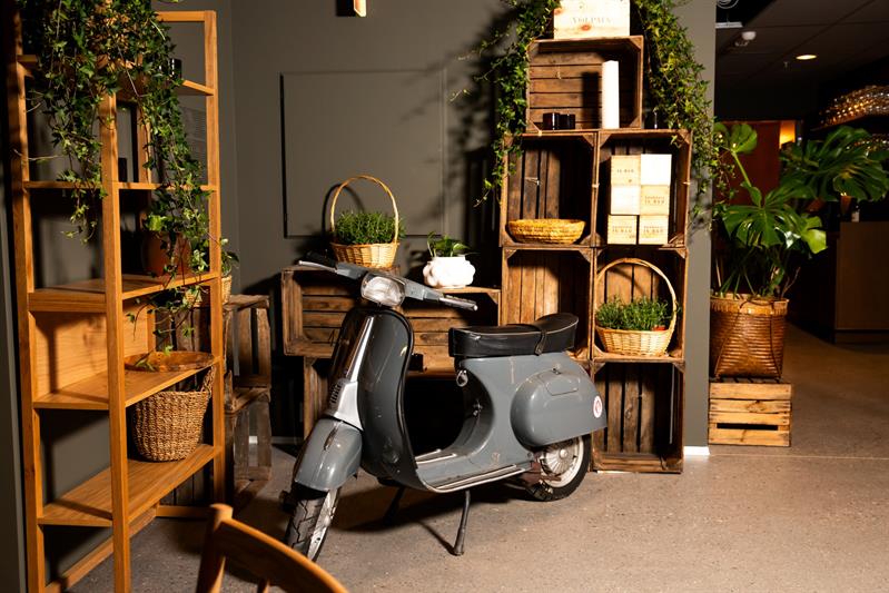 En moped som sto parkert inne på området foran hyller og kurver fylt med planter