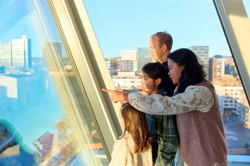En familie som ser ut over byen gjennom et panoramavindu