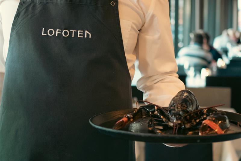 Mann i forkle som holder et brett med en hummer på