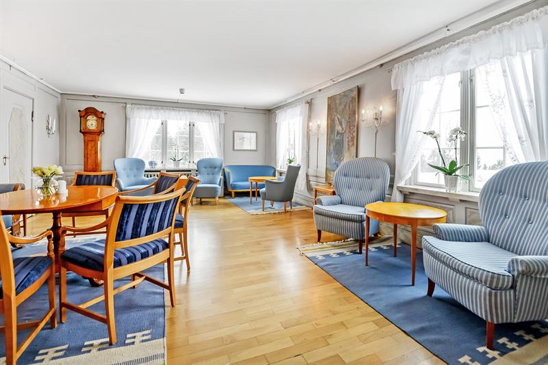 Stue med lenestoler, små bord og et gulvur.