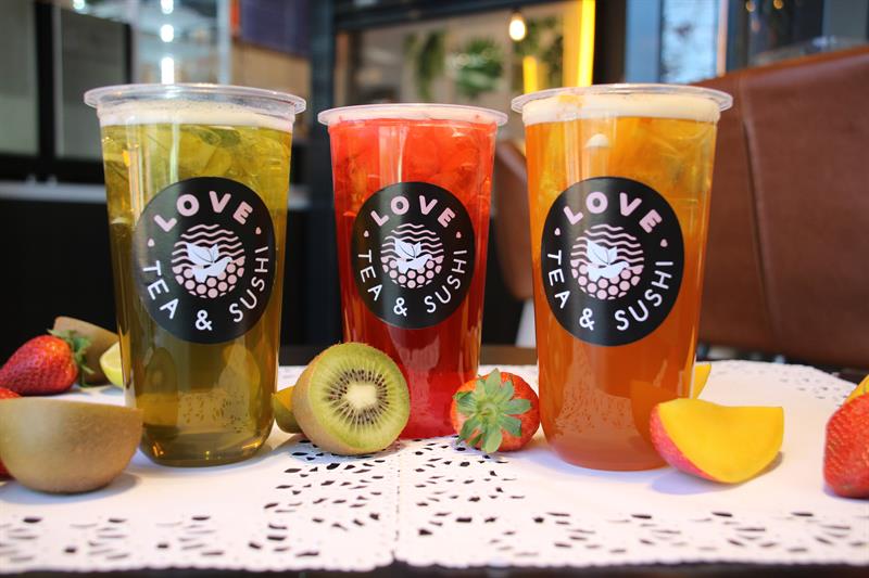 Nærbilde av tre glass med grønn, rød og oransje boblete med skiver av jordbær, kiwi og mango ved siden av.