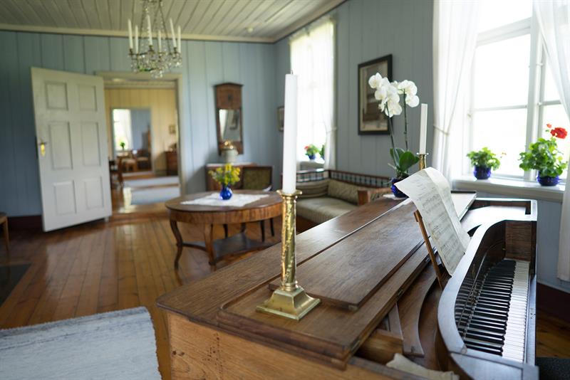 Interiør fra gammel trestue med piano, sitteseksjon og sofabord