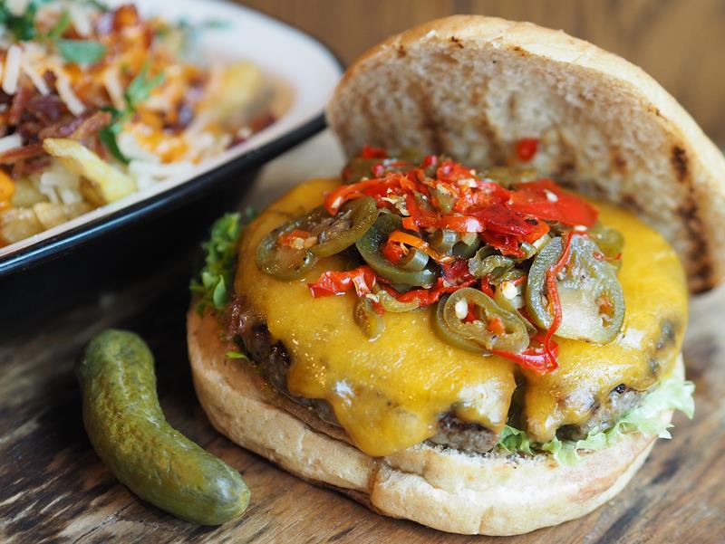 Detaljbilde av en cheeseburger med en sylteagurk ved siden av.