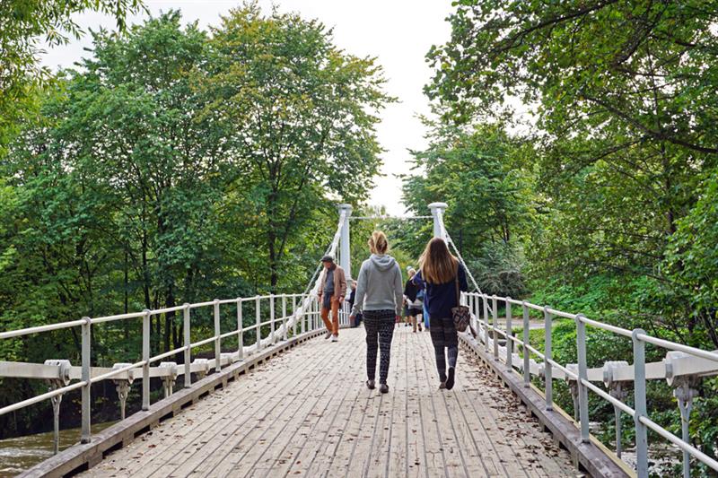 Broen en sommerdag. Folk som går på broen, grønne trær rundt omkring.