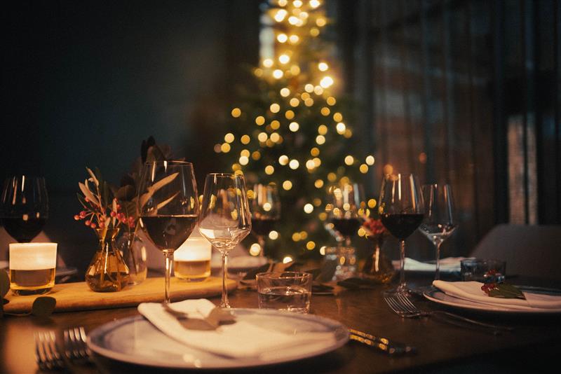 Et bord dekket til middag med vinglass og et juletre i bakgrunnen