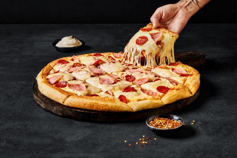 Detaljbilde av en pizza og en hånd som tar opp et stykke.
