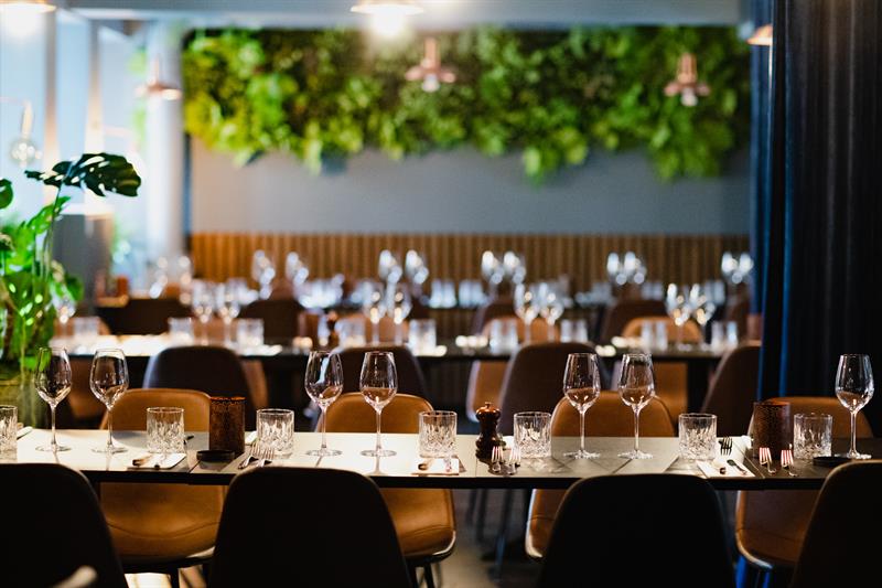 Lange bord dekket til middag, oransje stoler og planter langs veggen