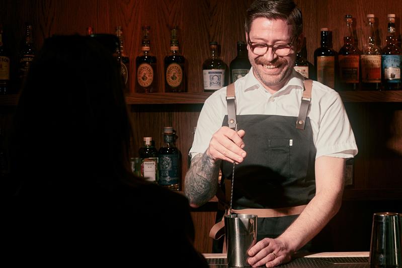 Bartender lager en cocktail bak baren mens en gjest sitter foran disken.
