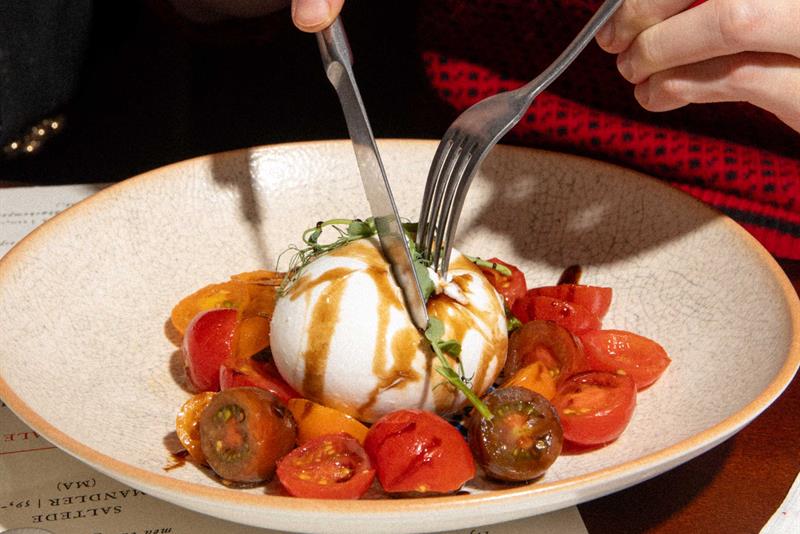En gjest skjærer opp en burrata som serveres med tomater og dressing på en restaurant