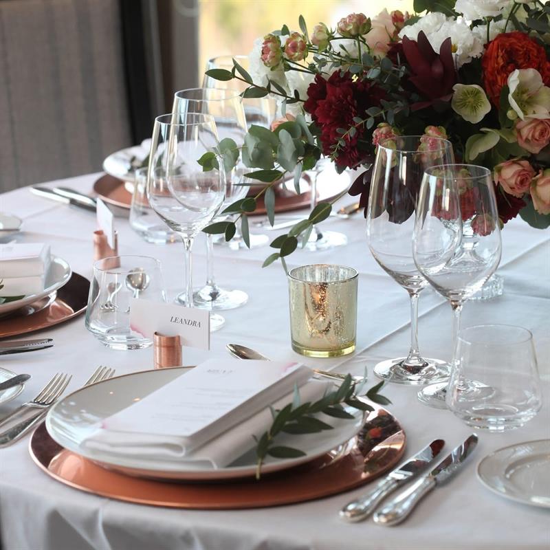 Stilig borddekking med blomster, vinglass og kobberdetaljer i en lys og elegant spisestue.