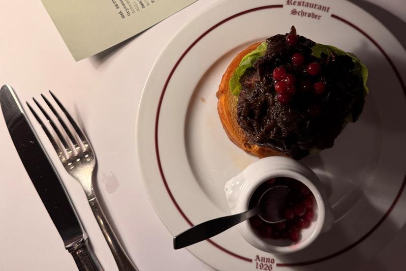 Åpent smørbrød med mørt kjøtt og tyttebær, servert på Restaurant Schrøder, med menyen i bakgrunnen.