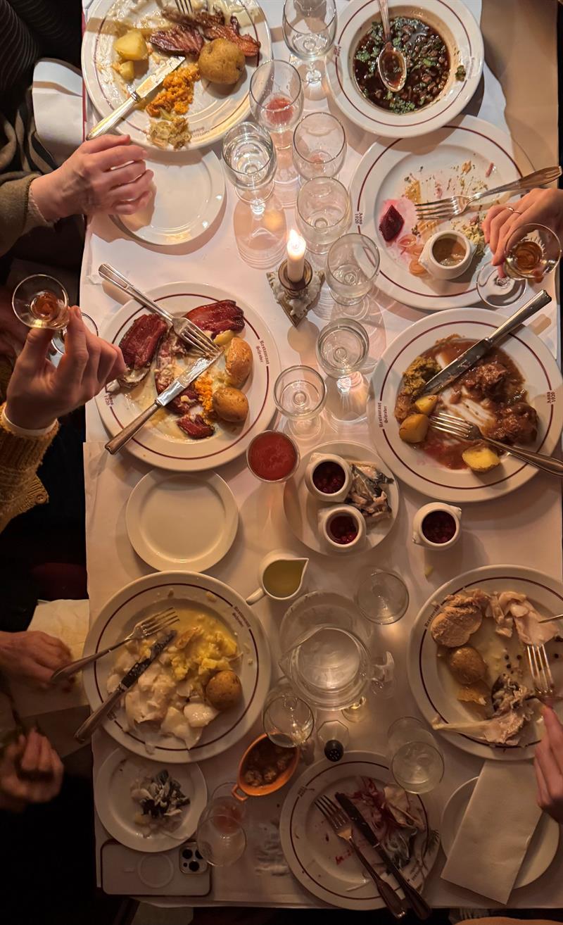 Et langt bord dekket med tradisjonelle norske retter, levende lys og gjester som spiser sammen på Restaurant Schrøder.