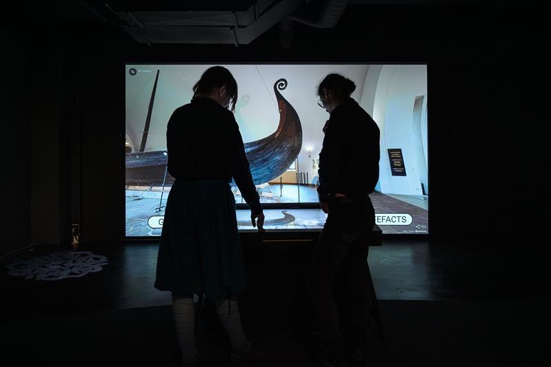 To personer interagerer med den digitale utstillingen fra Vikingskipshuset