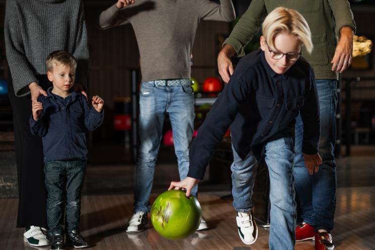 Et bowlende barn mens familien heier på ham i bakgrunnen