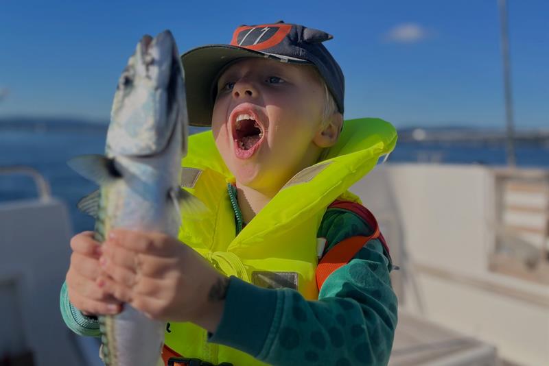 Et barn holder stolt opp en fisk de nettopp har fanget i båten.