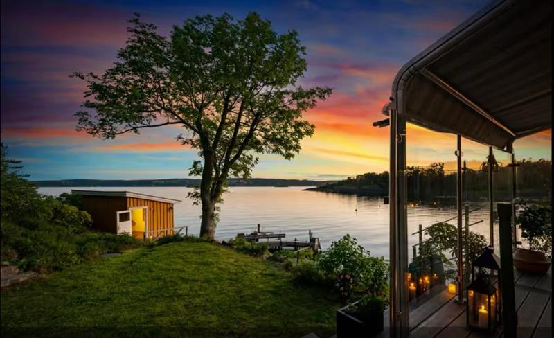 En fredelig kveld ved sjøen med utsikt over vannet, et tre og en opplyst hytte i solnedgangen.