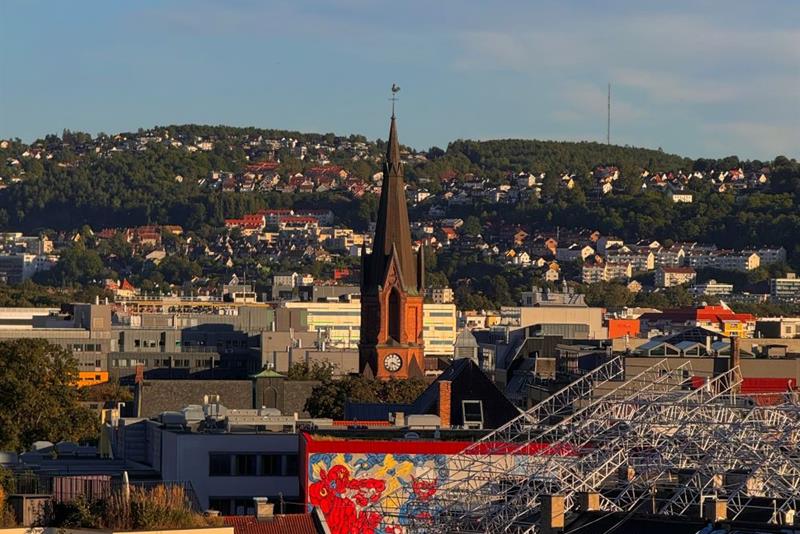 Utsikt over byen med kirketårn, hustak og en ås i bakgrunnen