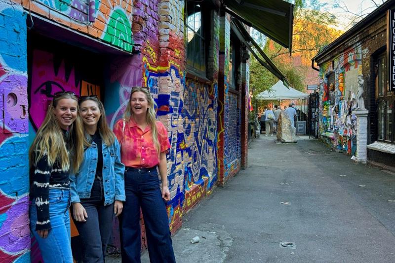 Tre jenter som står foran en vegg med graffiti på
