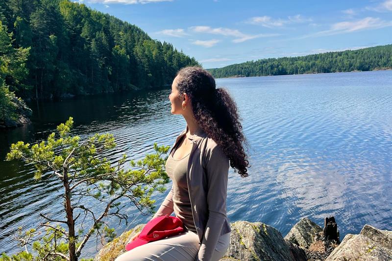 Jente som sitter ved en innsjø med skogen i bakgrunnen