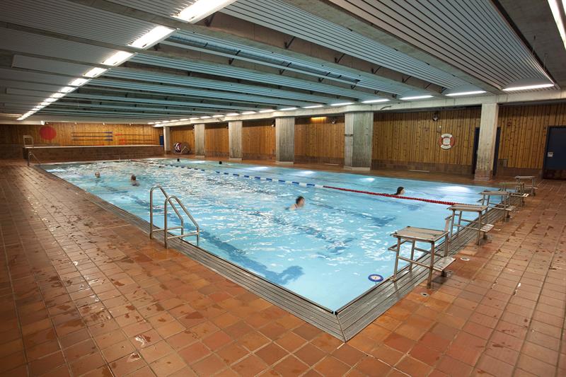 Innendørsbasseng med svømmere. Rødbrune fliser.