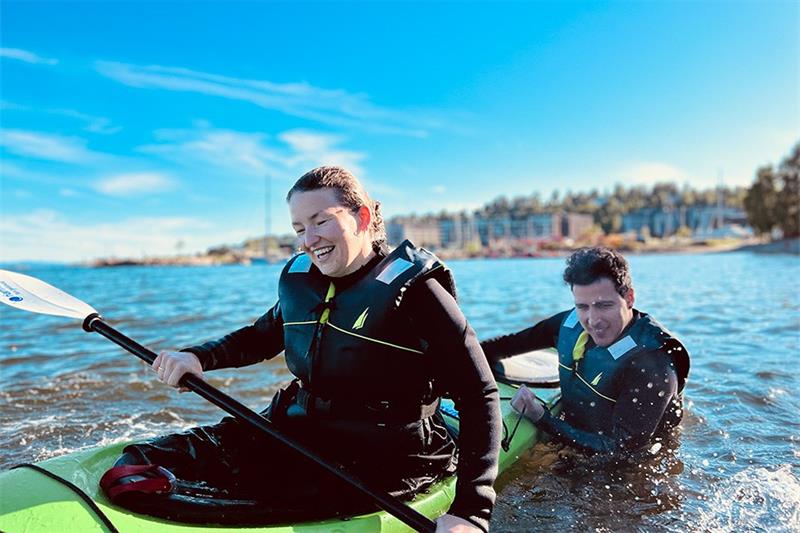 En kvinne som øver seg på å padle i vannet, mens en mann holder kajaken