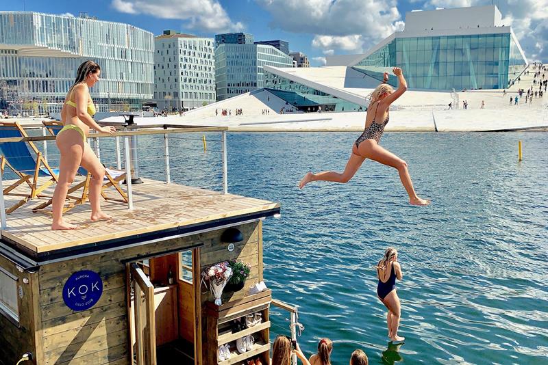 Folk som hopper i vannet med operaen i bakgrunnen.
